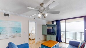 Ein Zimmer mit Deckenventilator, einem blauen Sofa, einem Holztisch und Blick auf den Balkon.