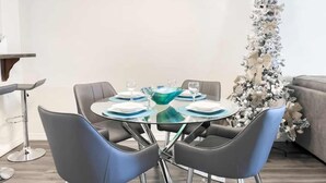 Un comedor moderno con una mesa redonda de vidrio, cuatro sillas negras y un árbol de Navidad al fondo.