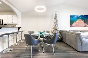 Une cuisine moderne avec des meubles blancs, un coin repas avec une table ronde et des chaises, un canapé gris et un sapin de Noël.