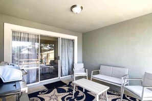 Une pièce dotée d’une porte-fenêtre coulissante donnant sur une terrasse, d’un canapé blanc, d’une petite table et d’un barbecue.