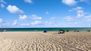 Una playa arenosa con tiendas de campaña y sombrillas, un cielo azul despejado y el océano al fondo.