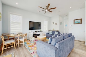 Ein modernes Wohnzimmer mit grauem Sofa, Holzesstisch und Deckenventilator.