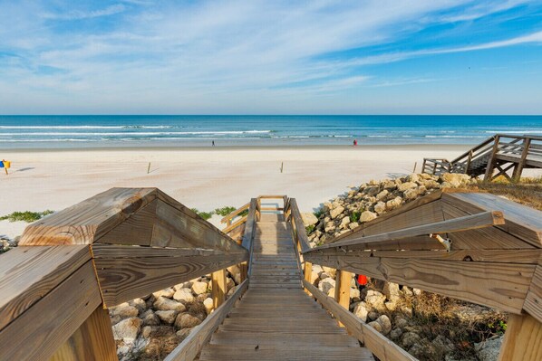 A wooden boardwalk leading to beach huts with a view of the ocean.