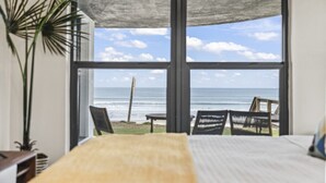 Une chambre dotée d’une grande fenêtre donnant sur une plage, avec un lit, une plante et une vue sur l’océan.