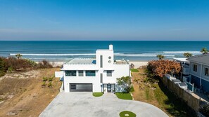 A modern two-story house with a garage, a driveway, and a view of the ocean.
