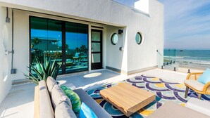 Een modern balkon met uitzicht op de oceaan, een zwembad en een loungehoek met een bank en een houten tafel.