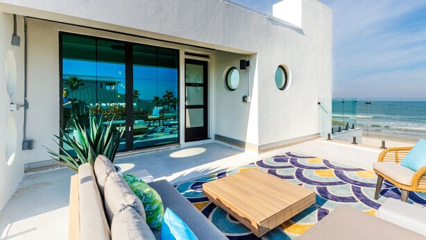 Un balcon moderne offrant une vue sur l’océan, avec une piscine et un espace détente comprenant un canapé et une table en bois.