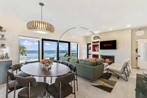 A modern living room with a fireplace, a large TV, and a view of the ocean.