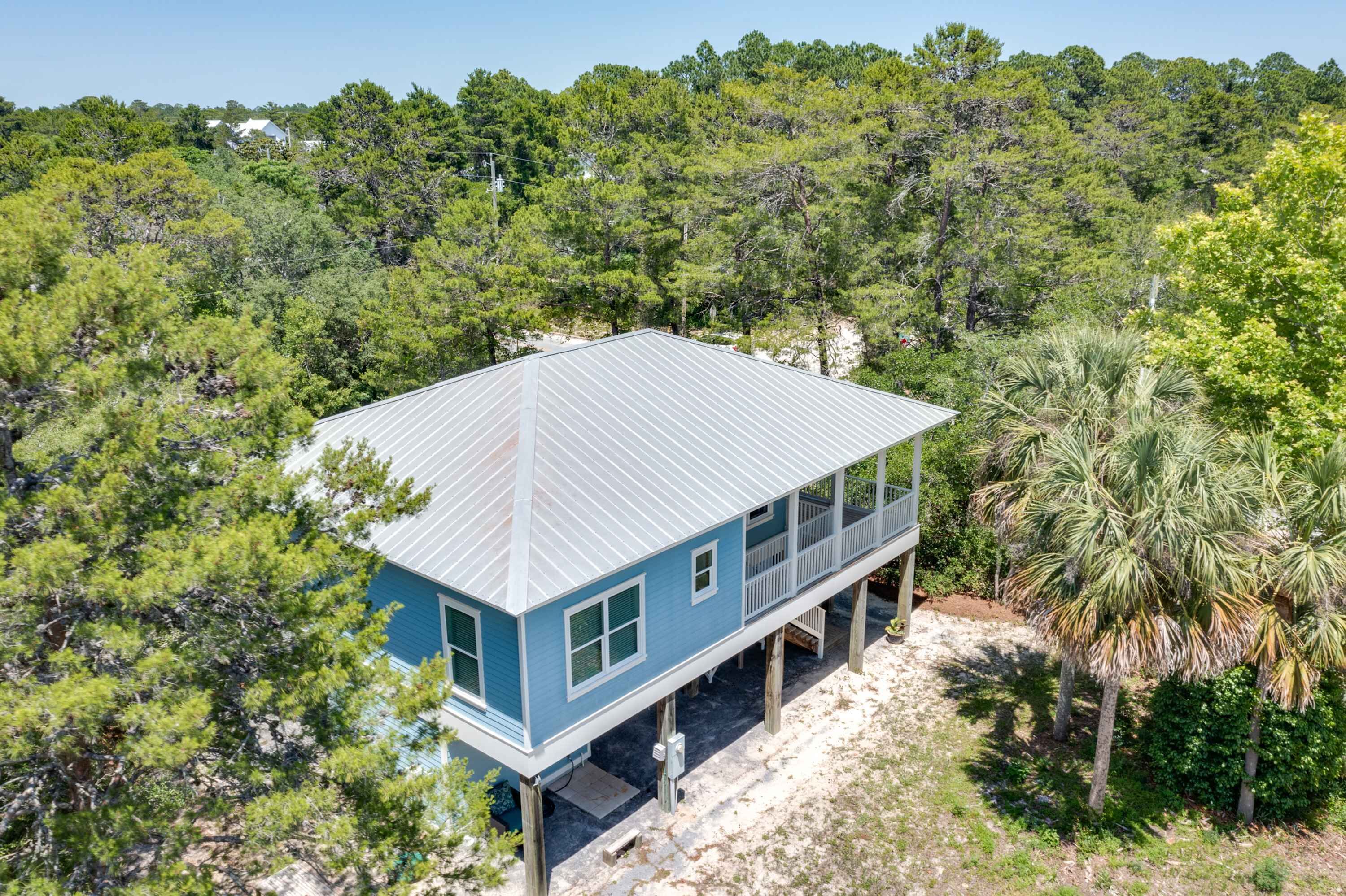 A two-story house with a metal roof, surrounded by dense forest and palm trees.