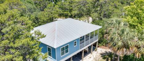 A two-story house with a metal roof, surrounded by dense forest and palm trees.