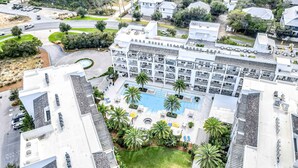 Vue aérienne d’un hôtel doté d’une cour intérieure, de nombreux balcons et d’une piscine entourée de palmiers.