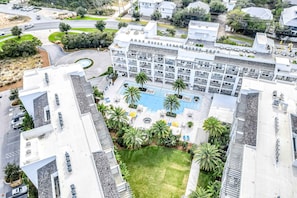An aerial view of a hotel with a central courtyard, multiple balconies, and a swimming pool surrounded by palm trees. - Chic condo steps from beach with patio, W/D, AC, and resort-style pool and gym (Inlet Beach)