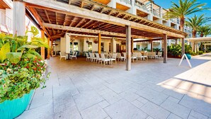 Un espace extérieur aménagé avec plusieurs tables et chaises, un coin salon abrité et une piscine.