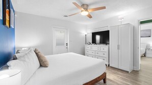 Ein Schlafzimmer mit einem Bett, einem Deckenventilator, einem Schminktisch und einem Fernseher.