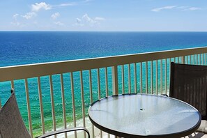 Un balcón con una mesa y sillas de vidrio, con vista al mar turquesa y un cielo despejado.