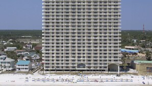 Een hoog hotel met meerdere balkons, gelegen nabij een strand met ligbedden en parasols.