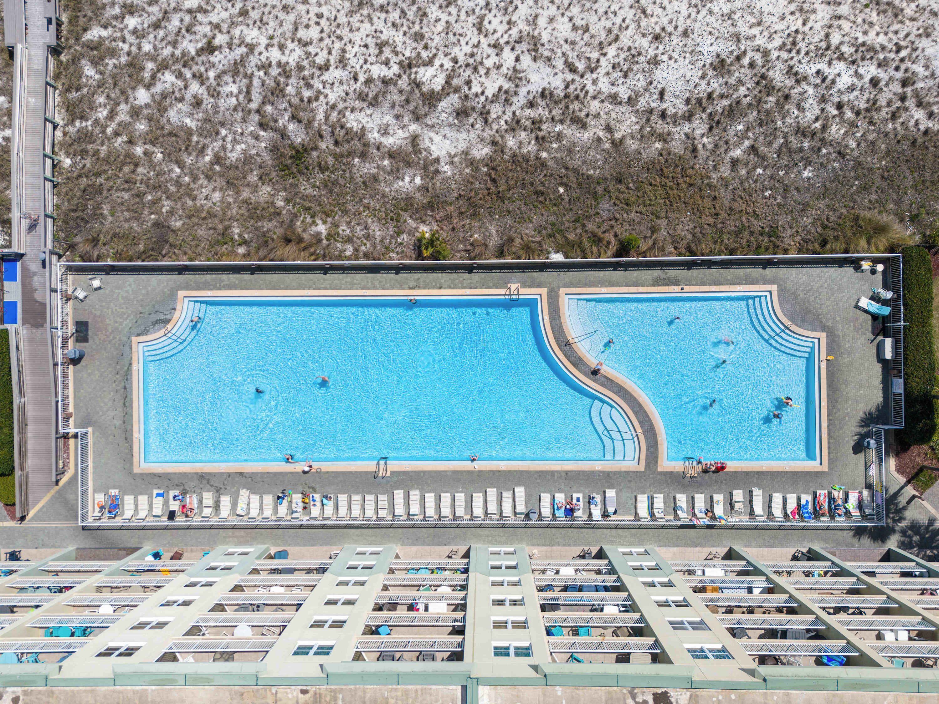 Vista aérea de un complejo de piscinas con varias albercas, camastros y una zona techada con asientos.