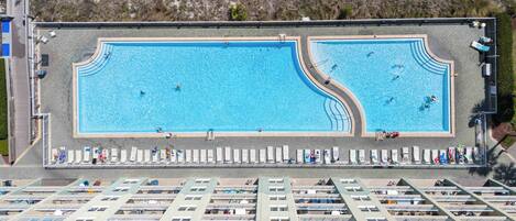Vista aérea de un complejo de piscinas con varias albercas, camastros y una zona techada con asientos.