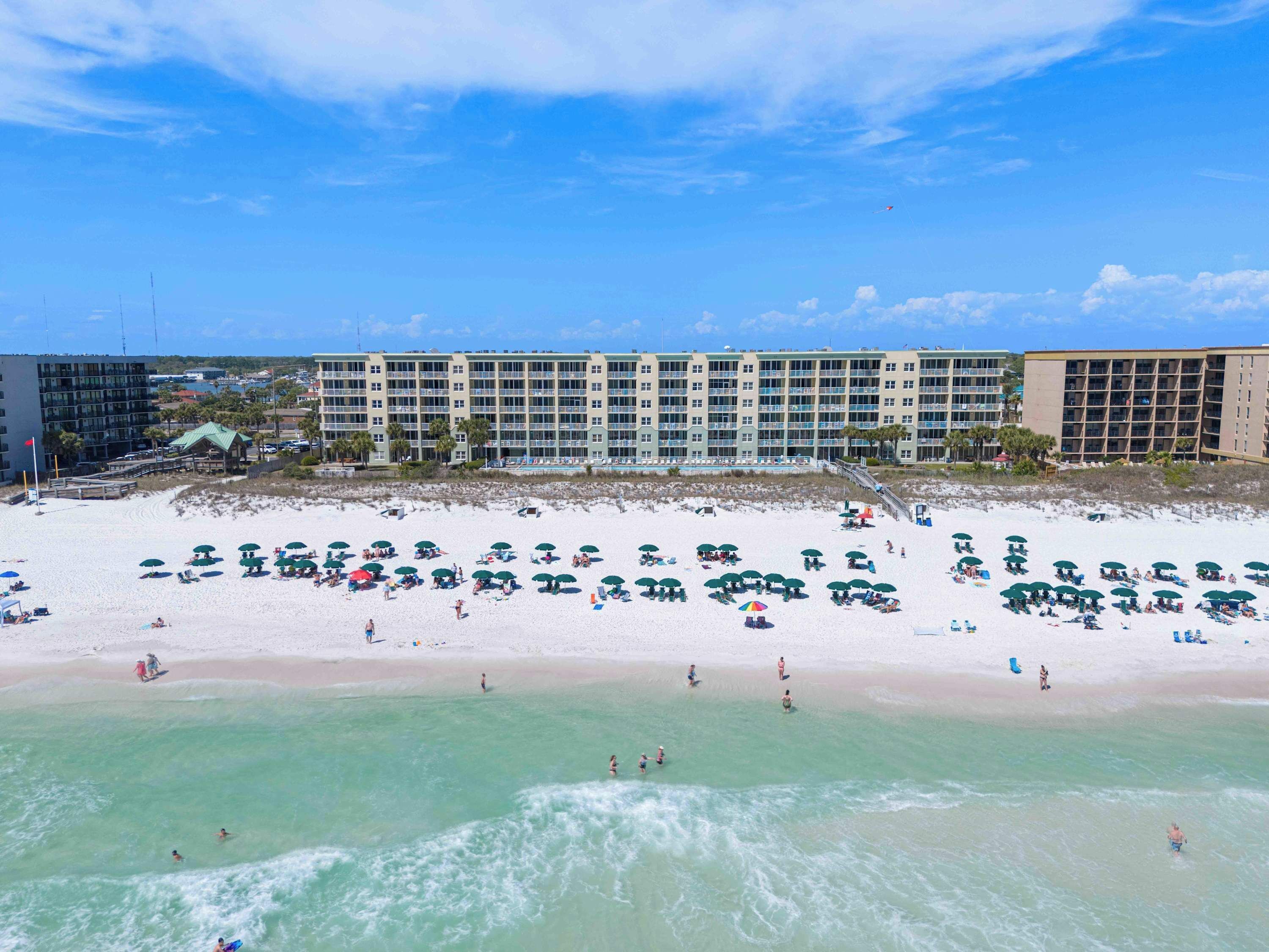 A beach resort with multiple levels of buildings, a sandy beach, and numerous umbrellas.