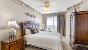 A bedroom with a large bed, a ceiling fan, a nightstand with a lamp, a dresser, and a window with curtains. - Sixth floor Summer Place condo w beach access, shared pool, and more (Fort Walton Beach)