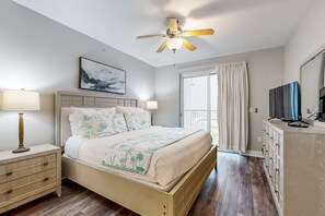 A bedroom with a bed, bedside tables, a ceiling fan, a TV, and a window with curtains. - Gulf-front condo with washer/dryer, pools, hot tub, fitness room, & beach access (Fort Walton Beach)