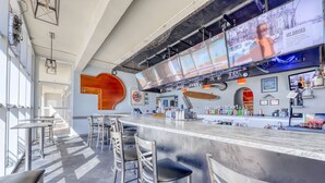 Um bar moderno com um balcão extenso, banquetas e uma tela grande exibindo uma pessoa.