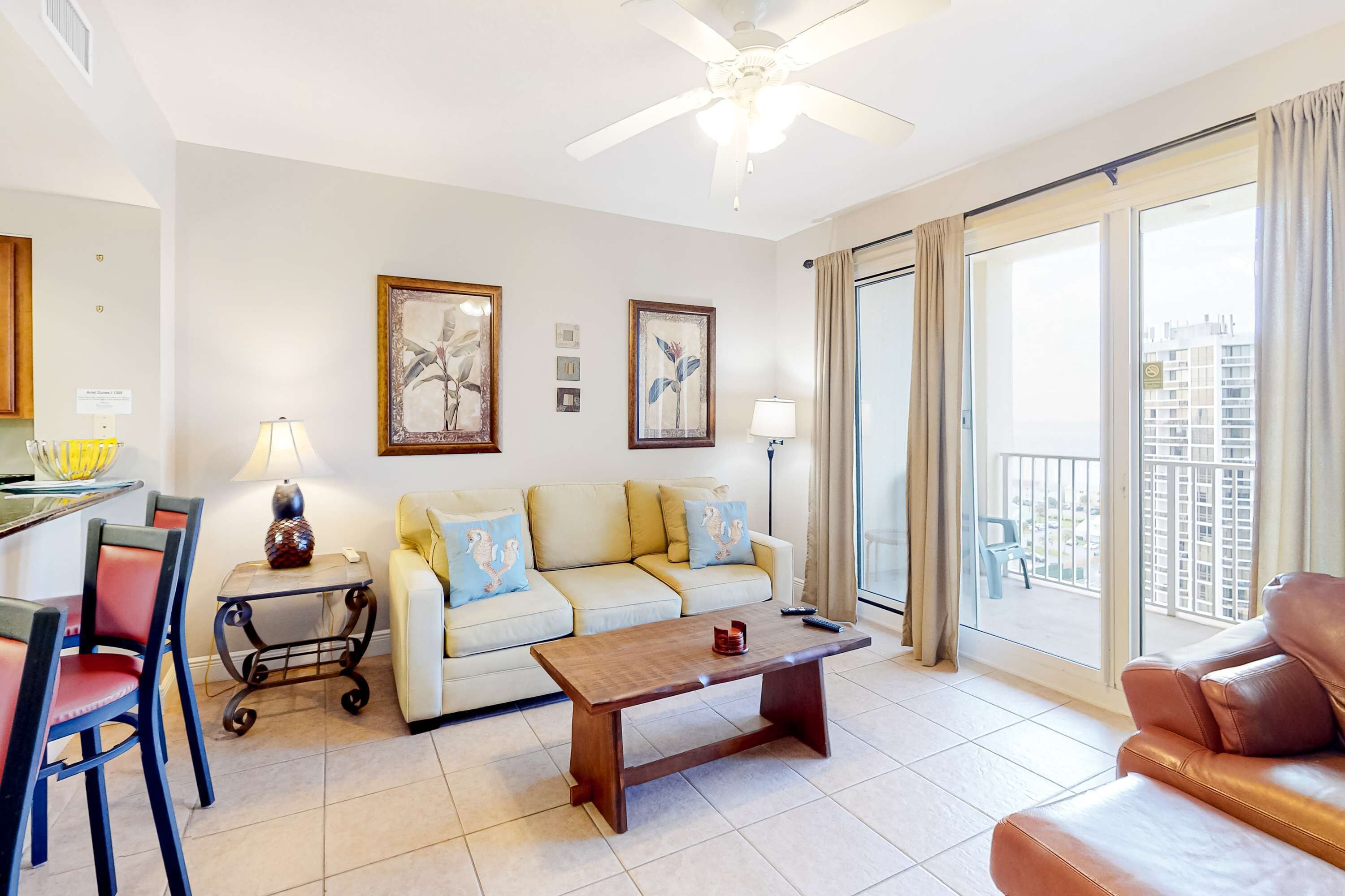 A living room with a sofa, a coffee table, a dining area with chairs, and a balcony with a view.