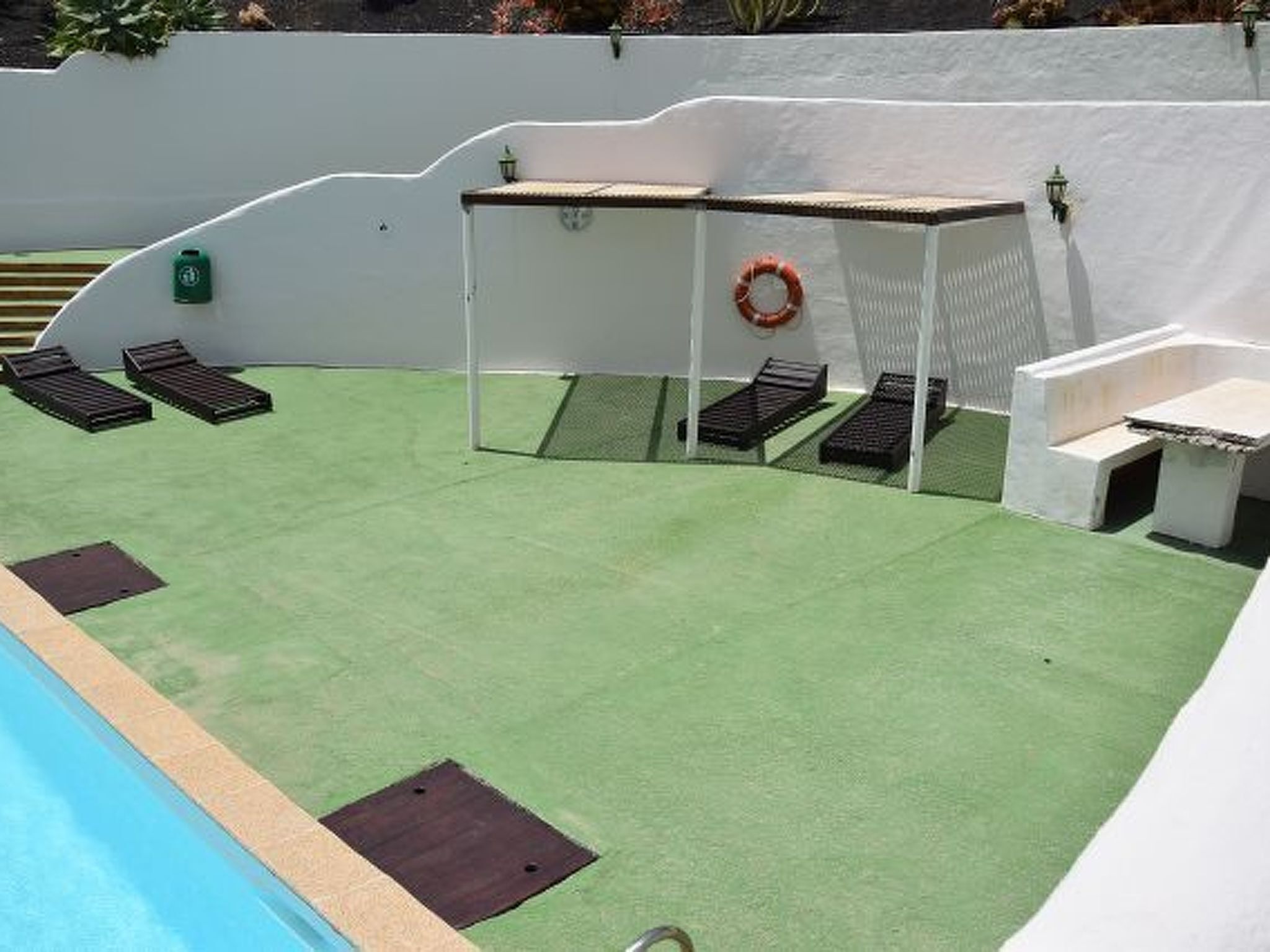 Zona de piscina con césped artificial, sillas de descanso, una mesita y un flotador.