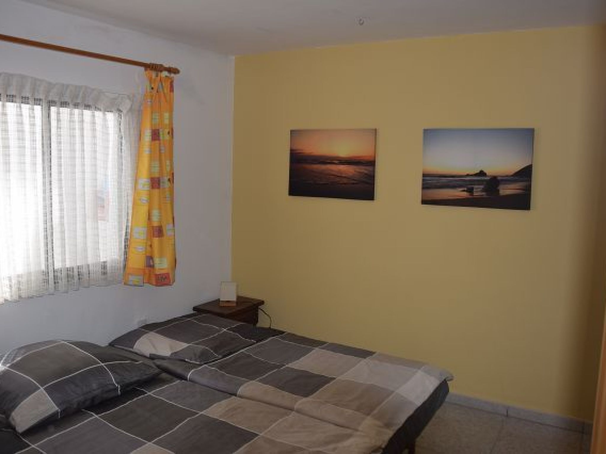 Un dormitorio con cama, cortinas y dos cuadros en la pared.