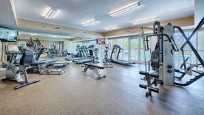 Una palestra con tapis roulant, macchinari per pesi e uno schermo televisivo.