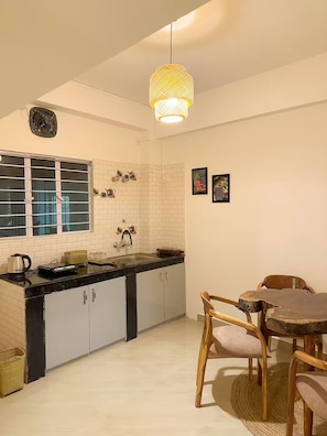 A kitchen with white tiled walls, a black countertop, and a wooden dining table with chairs.