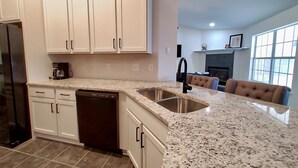 Una cucina con mobili bianchi, lavastoviglie, piano di lavoro in granito e lavello in acciaio inossidabile.