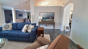 Un soggiorno con un divano blu, un divano marrone, un tavolino e un quadro appeso al muro.