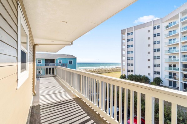 A balcony with a view of the beach and ocean, a building with multiple floors, and a clear sky. - Cozy coastal condo with pool, fast WiFi, central AC, & easy beach access (Pensacola Beach)