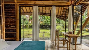 Una habitación con cama, una mesa y vistas a un jardín a través de amplios ventanales.