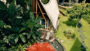 Una cabaña con techo de paja, rodeada de exuberante follaje y una zona con alfombra roja.