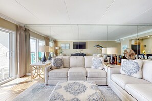 Ein modernes Wohnzimmer mit einem beigen Sofa, einem gemusterten Teppich und einem Essbereich mit Holztisch und Stühlen.