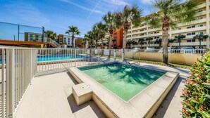 Una piscina con valla blanca, rodeada de palmeras y un edificio de varios pisos.