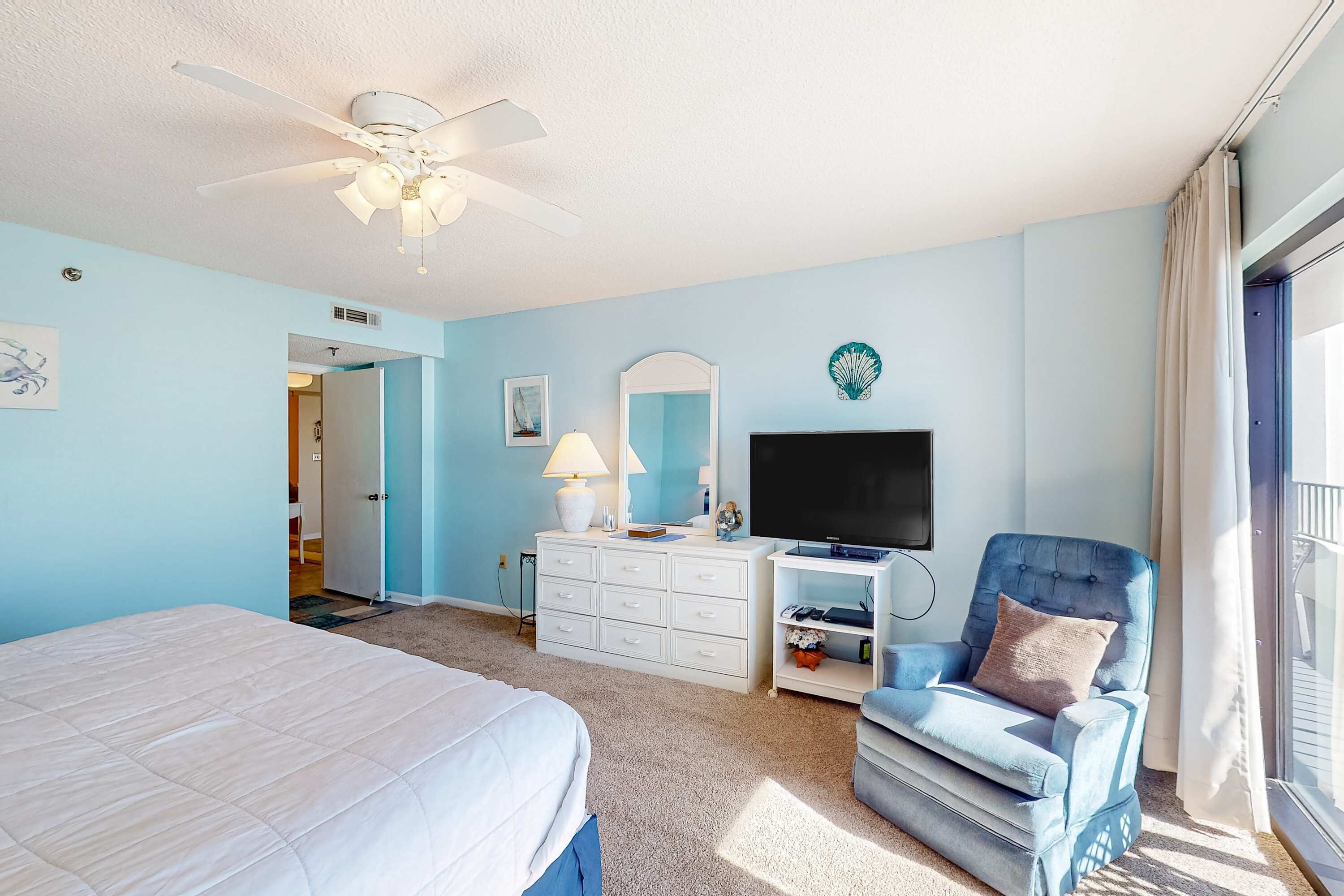 A bedroom with a bed, a dresser, a television, a chair, and a ceiling fan.