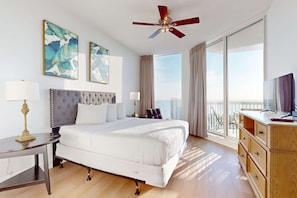 A spacious bedroom with a large bed, a ceiling fan, a view of the city, and a balcony with a table and chairs. - Gorgeous penthouse w shared outdoor pool, hot tub, tennis - Snowbird-friendly (Destin)
