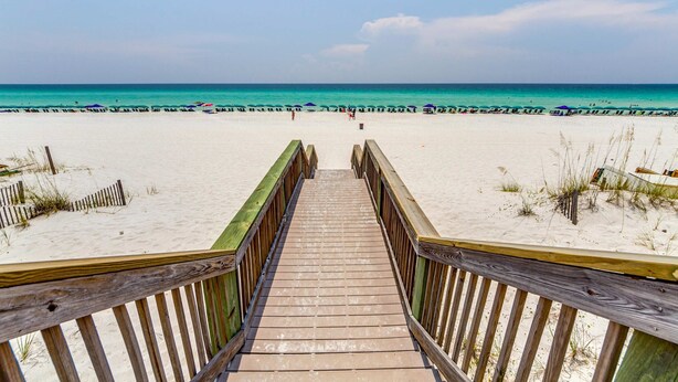 Un muelle de madera que conduce a una playa arenosa con vista despejada al océano.