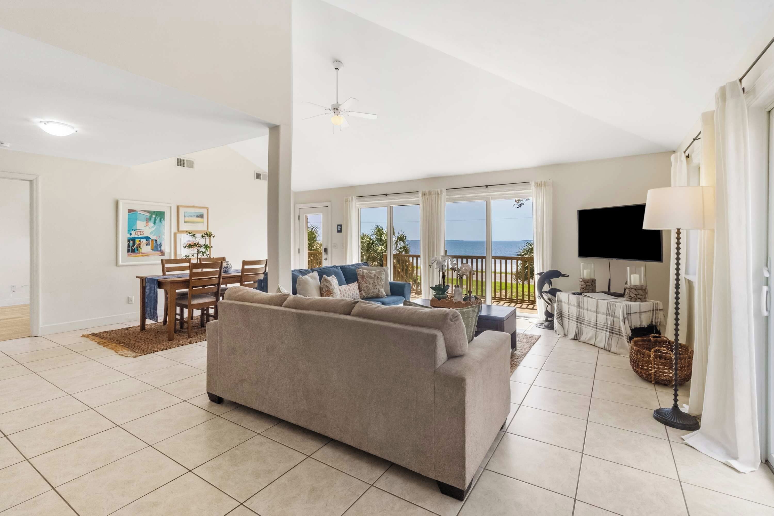 A spacious living area with a sofa, dining table, and chairs, a television, and a view of the sea.