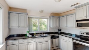 A kitchen with white cabinets, a black countertop, stainless steel appliances, and a window providing natural light. - Dog-friendly home with lovely water view, roomy deck, fast WiFi, central AC, W&D (Eastpoint)