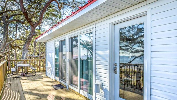 A wooden deck with a picnic table and a covered area, adjacent to a white building with large glass doors and windows. - Dog-friendly home with lovely water view, roomy deck, fast WiFi, central AC, W&D (Eastpoint)