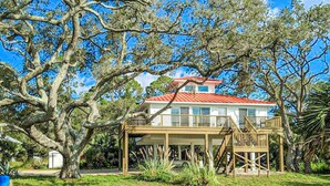 A two-story house with a red roof, surrounded by large trees and a grassy yard. - Dog-friendly home with lovely water view, roomy deck, fast WiFi, central AC, W&D (Eastpoint)