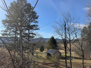 Paisagem rural com uma casa pequena cercada por árvores e campos abertos.