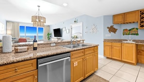 A modern kitchen with granite countertops, stainless steel appliances, wooden cabinets, and a view of the ocean. - Bright beach condo with water views & private balcony - pool, gym & beach (Destin)