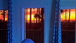 Een kamer met uitzicht op een zonsondergang door een raam, gordijnen en een bank.