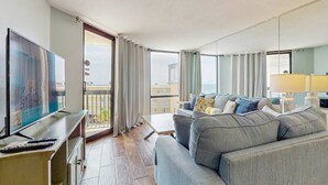 En moderne stue med et stort fladskærms-tv, en grå sofa og en balkon med gardiner.