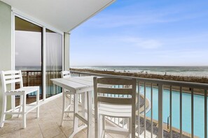 Un balcon avec des meubles blancs, une piscine et une vue sur la plage.